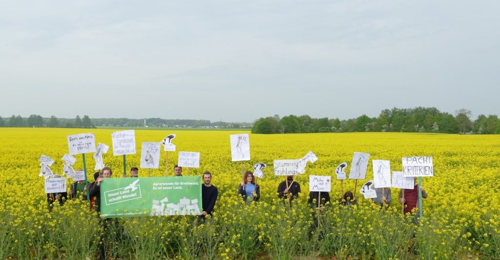 Unser Land schafft Wandel - mit schildern im Rapsfeld für bessere Landvergabe